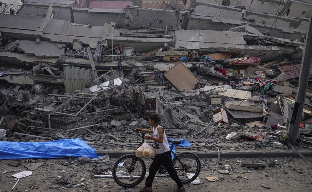 Un niño camina con una bicicleta junto a los restos de un edificio alcanzado por un ataque aéreo en Ciudad de Gaza. Foto: AP