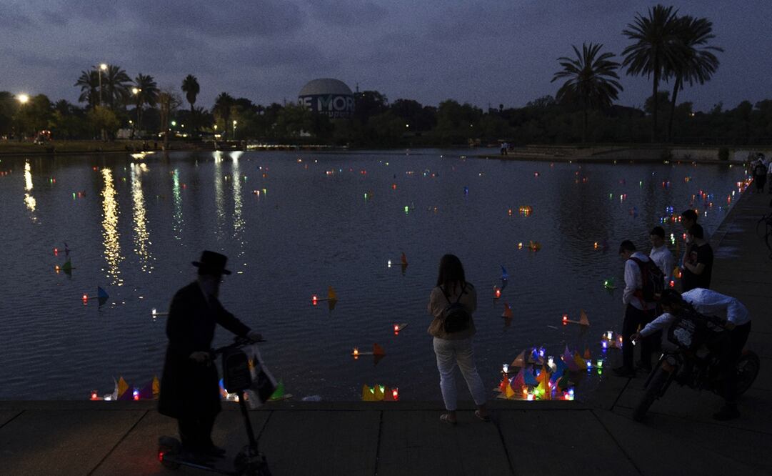 Personas observan los botes flotantes hechos a mano iluminados con velas y con los nombres de los campos de concentración nazis. Foto: AP/Oded Balilty