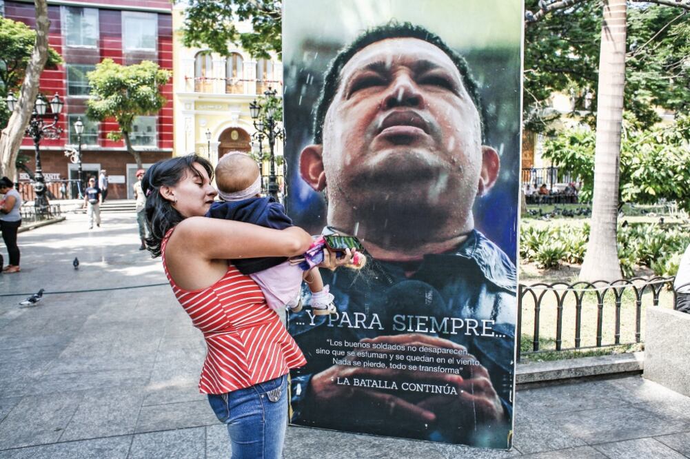 Una mujer con su bebé se detiene ante una imagen del fallecido presidente venezolano, Hugo Chávez, colocada en la Plaza Bolívar después de su retiro de la Asamblea Nacional (AN) (BORIS VERGARA. XINHUA)