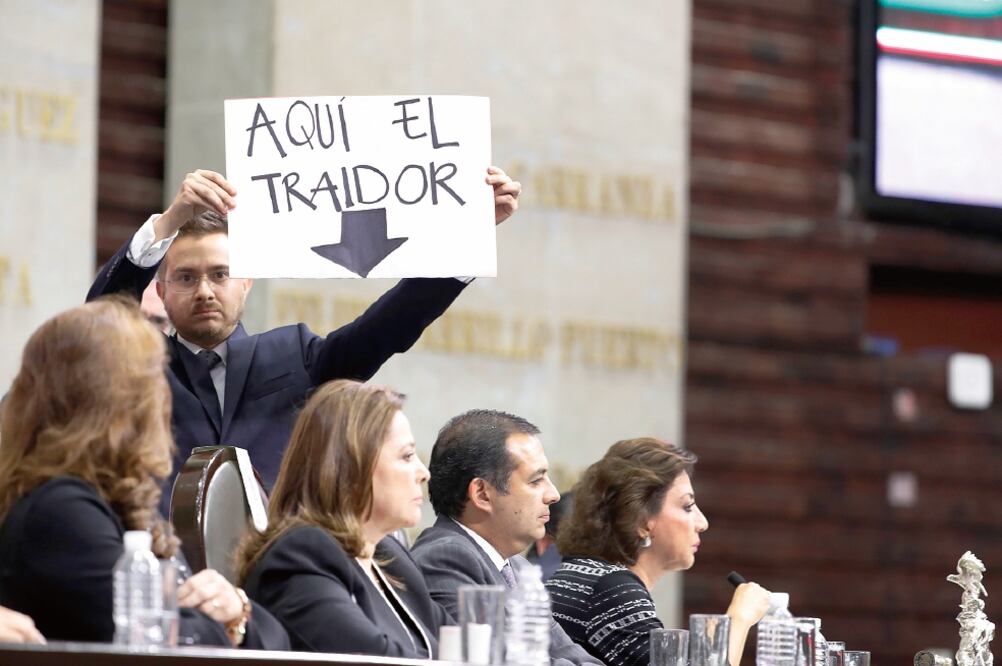 El diputado Santiago Torreblanca se paró atrás de Ernesto Cordero y mostró una cartulina con una flecha que apuntaba hacia él: "Traidor". (LUIS CORTÉS. EL UNIVERSAL)