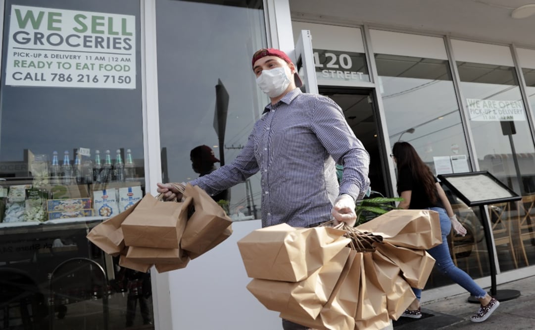 A restaurant employee wears a protective mask as he carries freshly made meals for delivery - Photo: Lynne Sladky/AP