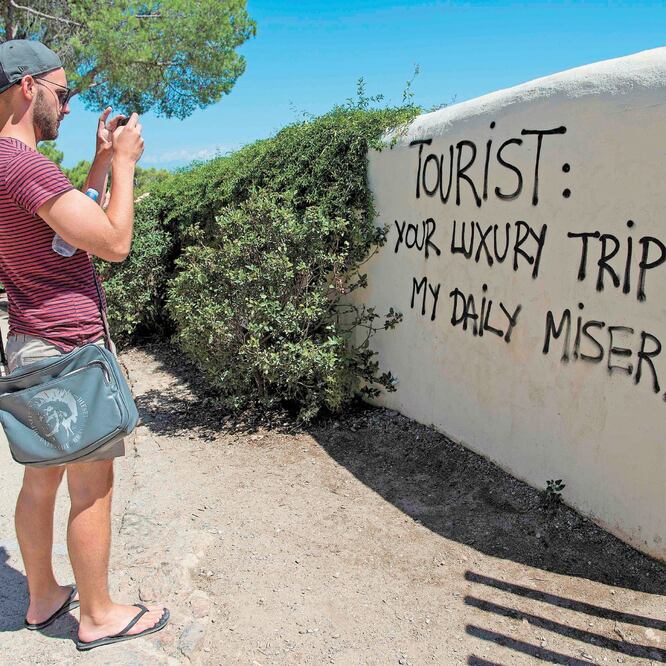 Un hombre toma una fotografía de un grafiti con la leyenda: “Turista: tu viaje lujoso es mi miseria diaria”, en Barcelona, en 2017. JOSEP LAGO. AFP