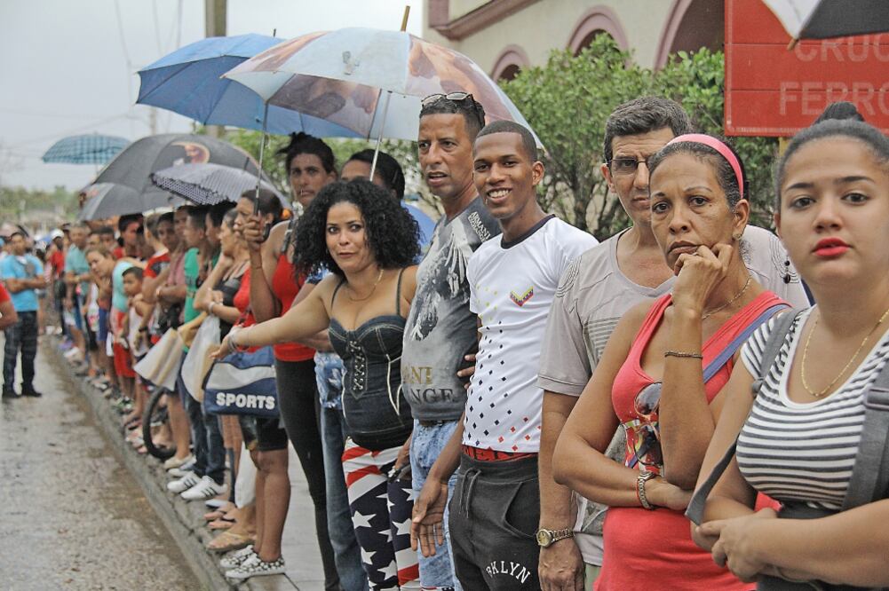 Un grupo de cubanos espera bajo la lluvia para ver pasar el convoy presidencial de Obama, en La Habana. ROLANDO PUJOL. EFE
