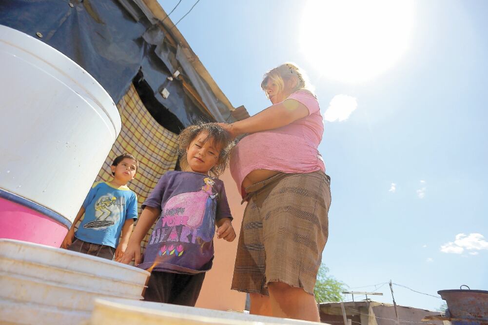 Mariela Rodríguez refresca a una de sus hijas con un poco de agua en la cabeza, dice que no puede tirar el líquido porque la pipa que les surte va sólo dos veces a la semana y le debe alcanzar para lavar, bañarse y preparar la comida. Foto: AMALIA ESCOBAR