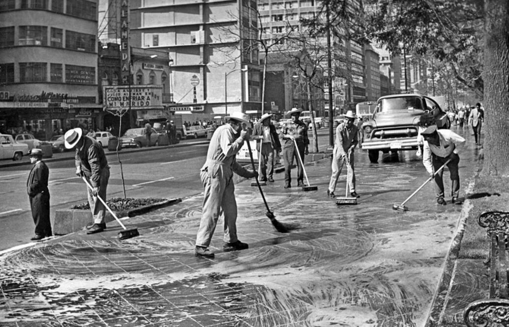 Un grupo de trabajadores del Departamento del Distrito Federal lava las banquetas de la Alameda Central en los años sesenta. Del lado izquierdo se aprecia el cine Alameda, ubicado entre Luis Moya y José María Marroqui, inaugurado en 1936; hoy se conserva únicamente la fachada. La marquesina anunciaba la cinta "Cómo enfriar a mi marido", de 1967. Más adelante se encuentran el templo de Corpus Christi y el Conjunto Alameda. Crédito: Archivo El Universal
