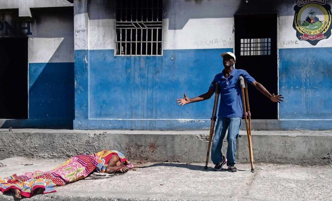 Un hombre, junto al cuerpo sin vida de una persona en los exteriores de la comisaría de Carrefour Aéroport, que fue incendiada la noche del 4 de marzo por miembros de pandillas, en Puerto Príncipe, Haití. Foto: Johnson Sabin / EFE