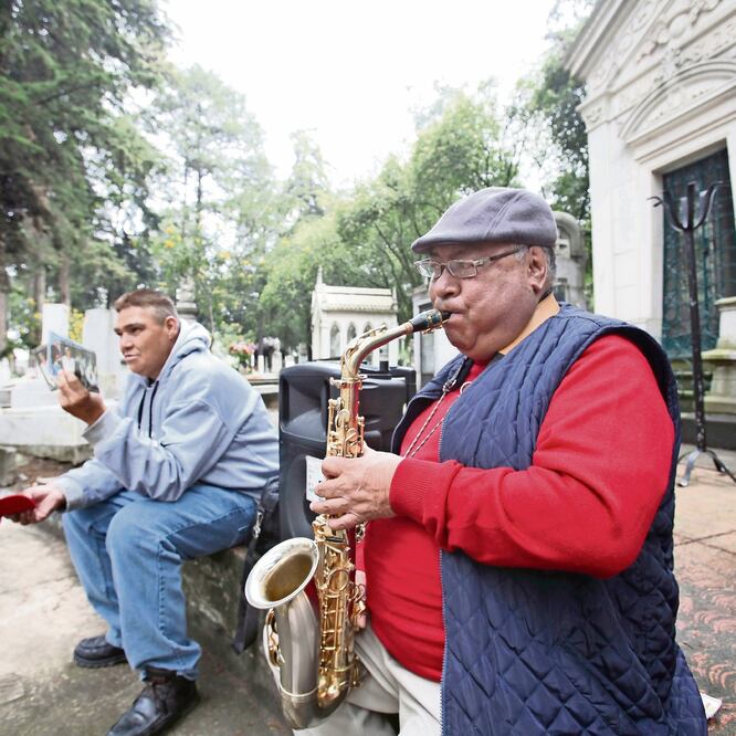 El saxofonista Romualdo García Zárate toca piezas que compuso en un obelisco del Panteón La Soledad; un amigo lo acompaña para recibir dinero. Foto: JORGE ALVARADO. EL UNIVERSAL