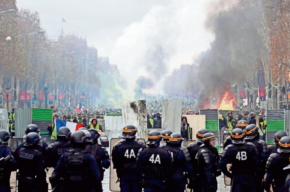 Manifestantes franceses en contra del alza en los precios del combustible gritan consignas a la policía durante los disturbios en los Campos Elíseos, en París. (GONZALO FUENTES. REUTERS)