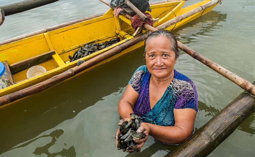 Gloria Temporada, de 59 años, muestra su captura de mejillones en Tángub, Filipinas, recolectados en bancos costeros poco profundos que emergen con la marea. Estos bancos son solo uno de los muchos entornos diversos en los que se practica la pesca a pequeña escala.  |  CRÉDITO: © FAO / DAVID HOGSHOLT