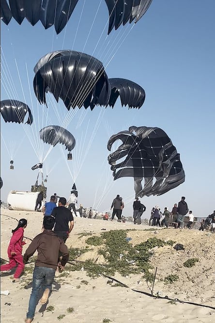Palestinos corriendo hacia paracaídas sujetos a paquetes de alimentos, lanzados desde aviones estadounidenses en una playa de la Franja de Gaza el 2 de marzo de 2024. Foto: Ilustrativa / AFP