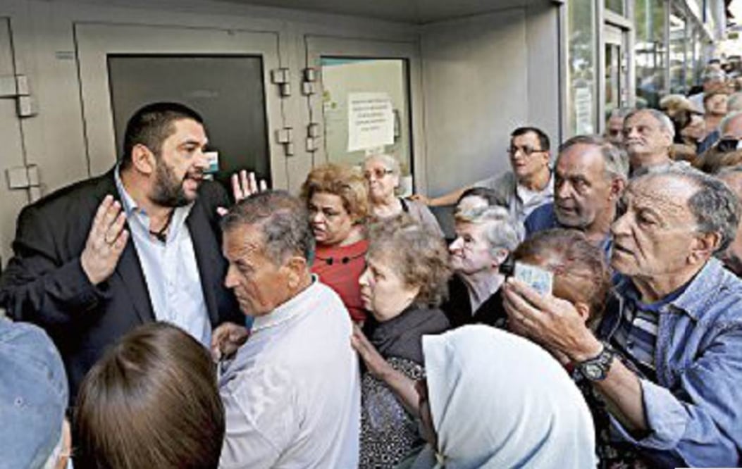 El gerente de un banco habla con pensionados que esperan poder sacar dinero en esa sucursal, en Atenas. Foto Reuters