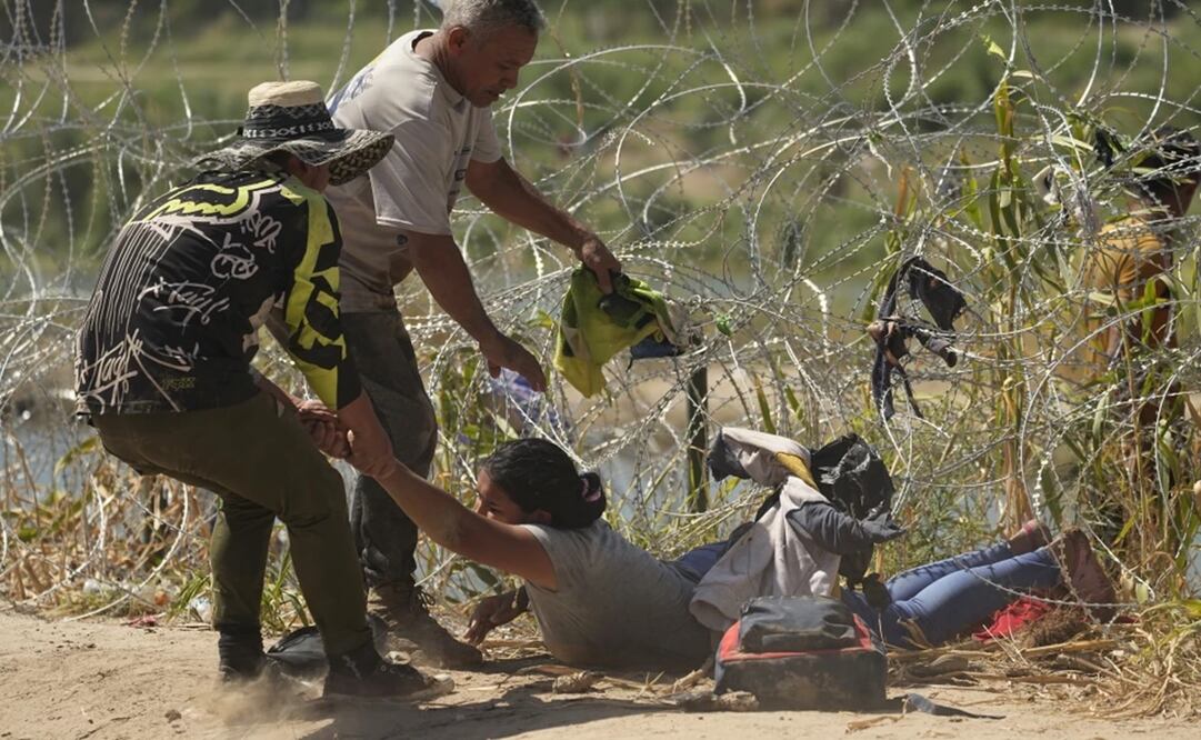 Una inmigrante que cruzó a Estados Unidos desde México es auxiliada a pasar debajo de alambre de púas en una de las márgenes del río Bravo, el jueves 21 de septiembre de 2023, en Eagle Pass, Texas. Foto: AP