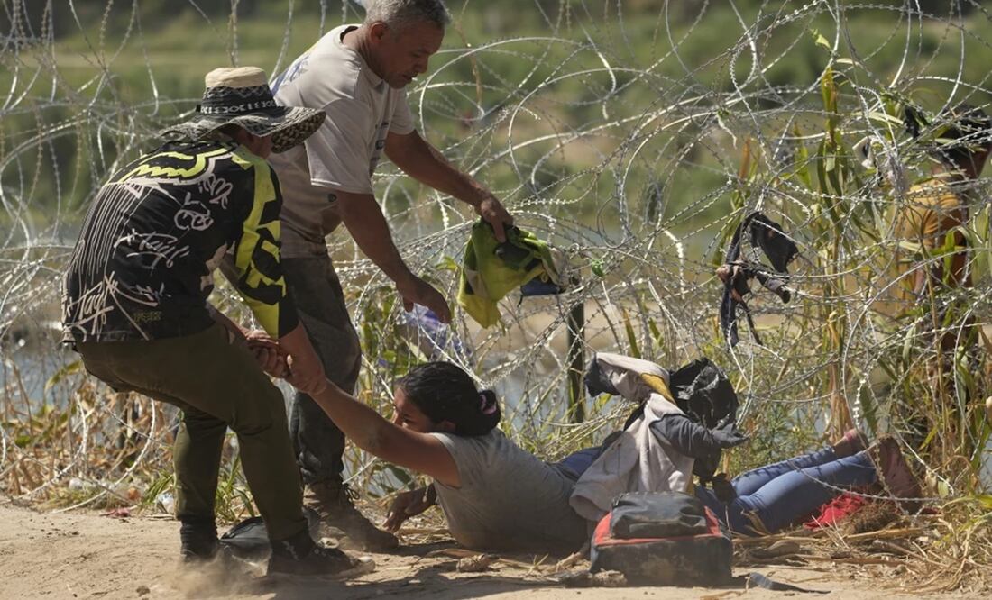 Una inmigrante que cruzó a Estados Unidos desde México es auxiliada a pasar debajo de alambre de púas en una de las márgenes del río Bravo, el jueves 21 de septiembre de 2023, en Eagle Pass, Texas. Foto: AP