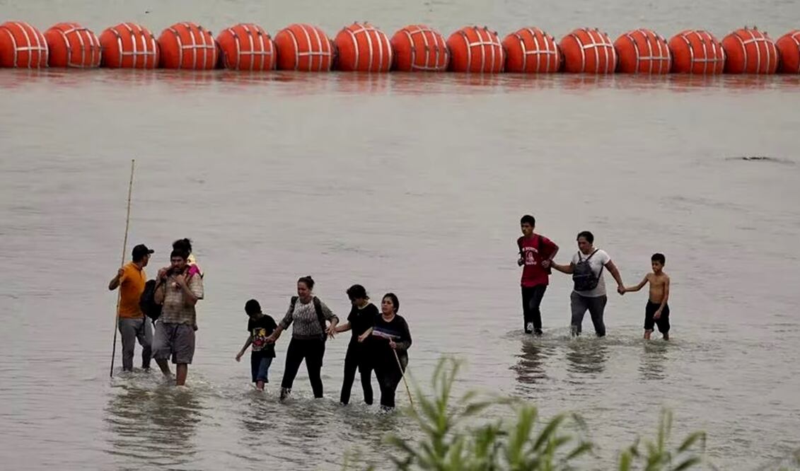 Migrantes que cruzan por el río Bravo caminan frente a enormes boyas colocados como una barrera fronteriza flotante. Foto: AP archivo/EL UNIVERSAL