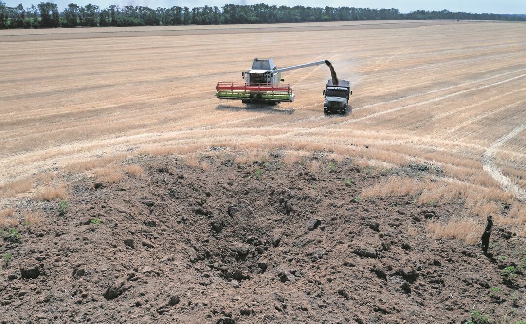 Un cráter dejado por un ataque con cohetes rusos, mientras un agricultor recolecta la cosecha en un campo que está a 10 kilómetros de la línea del frente, en Dnipropetrovsk.