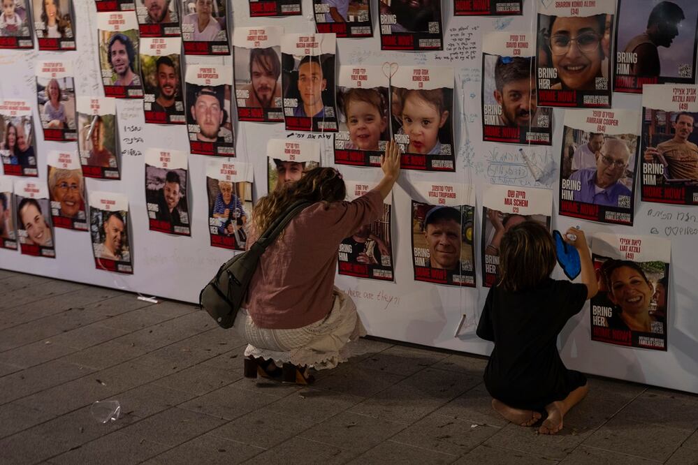 Una mujer israelí toca con la mano fotografías de israelíes desaparecidos y cautivos en Gaza, exhibidas en una pared en Tel Aviv. Foto: AP