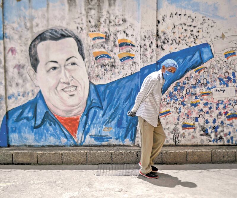 Recuerd o. Un hombre con un cubrebocas pasa junto a un mural del fallecido presidente de Venezuela, Hugo Chávez, ayer en Caracas. FEDERICO PARRA. AFP