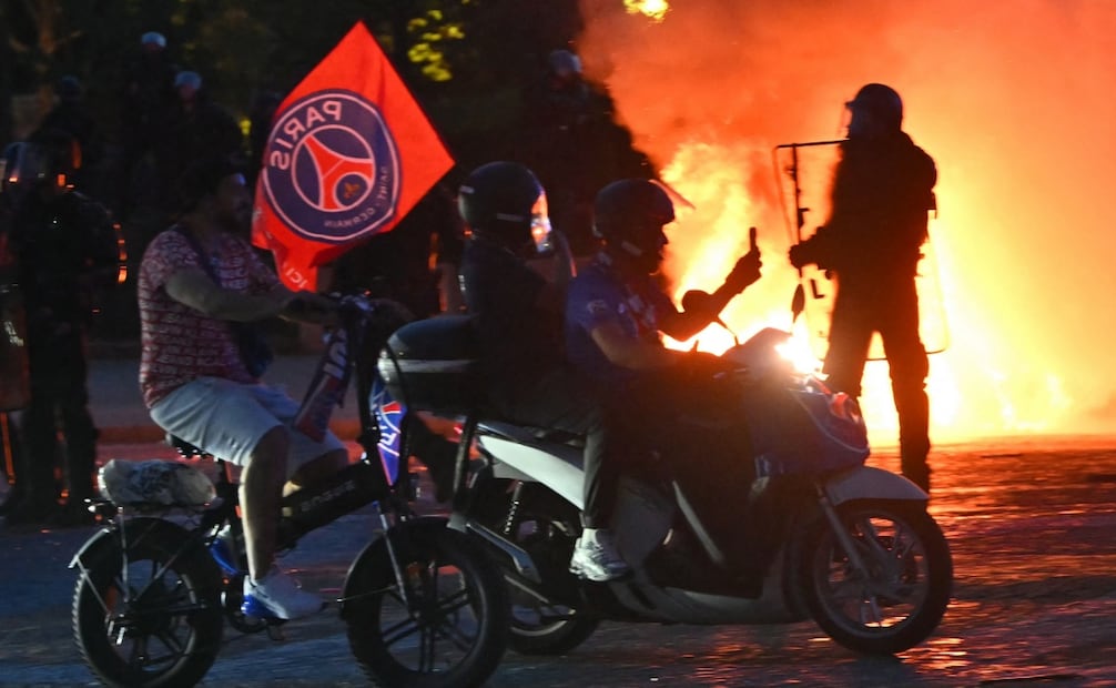 Aficionados del PSG circulan en moto frente a policías antidisturbios en París, tras ganar la final de la Liga de Campeones (30/05/2026). Foto: AFP