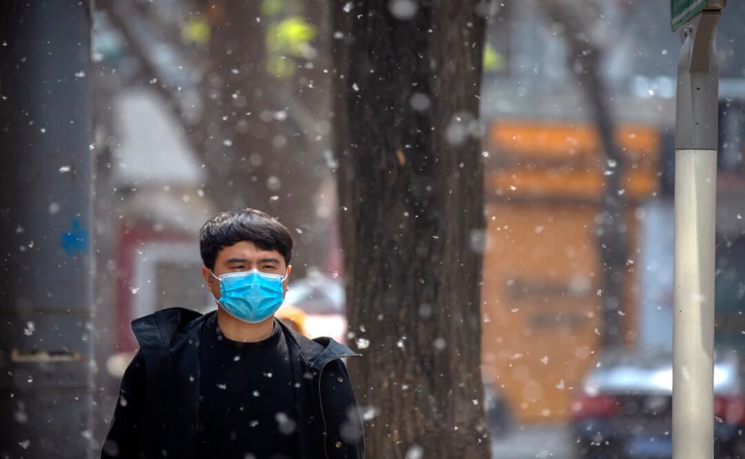A man wearing a face mask to help stop the spread of the coronavirus is surrounded by catkin fluff as he walks along a street in Beijing - Photo: Mark Schiefelbein/AP