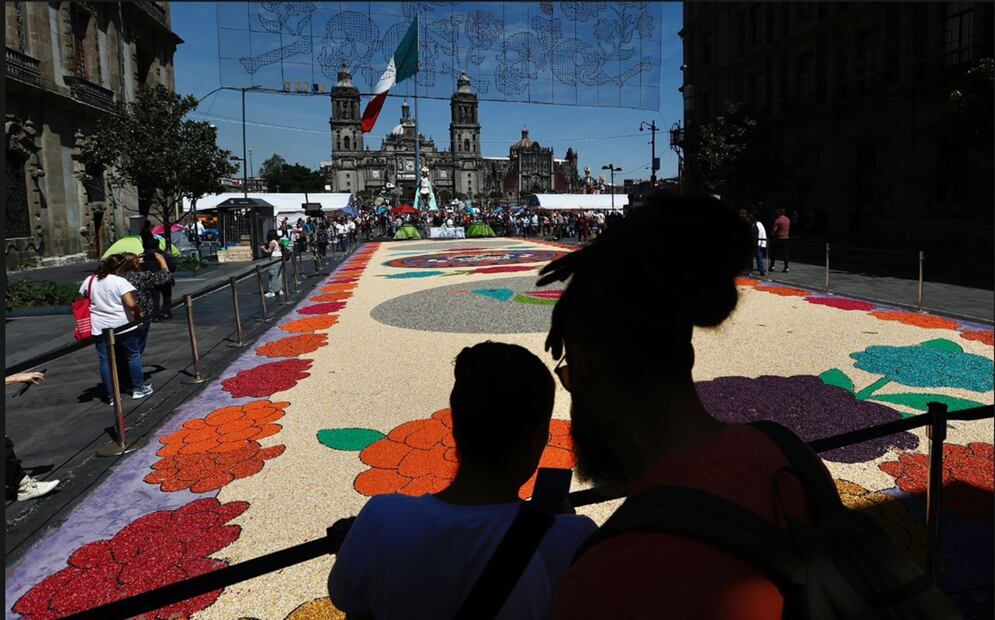 Visitantes se toman fotos frente al tapete monumental de 10 metros de ancho y 45 de largo elaborado con 80 por ciento de maíz natural que se ha instalado en el Zócalo capitalino, el 27 de octubre de 2025. Foto: Berenice Fregoso/EL UNIVERSAL