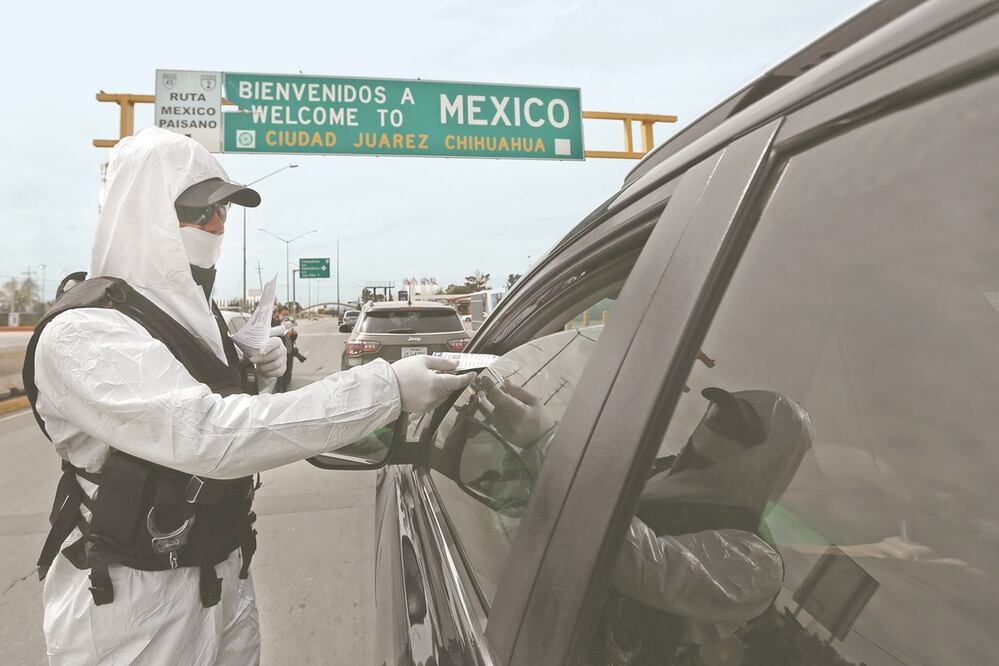 En Ciudad Juárez, Chihuahua, agentes de la Policía Vial vestidos con trajes especiales entregan folletos informativos sobre el virus a automovilistas que atraviesan la frontera de EU hacia México, sin mayor control sanitario. Foto: CHRISTIAN TORRES. EL UN