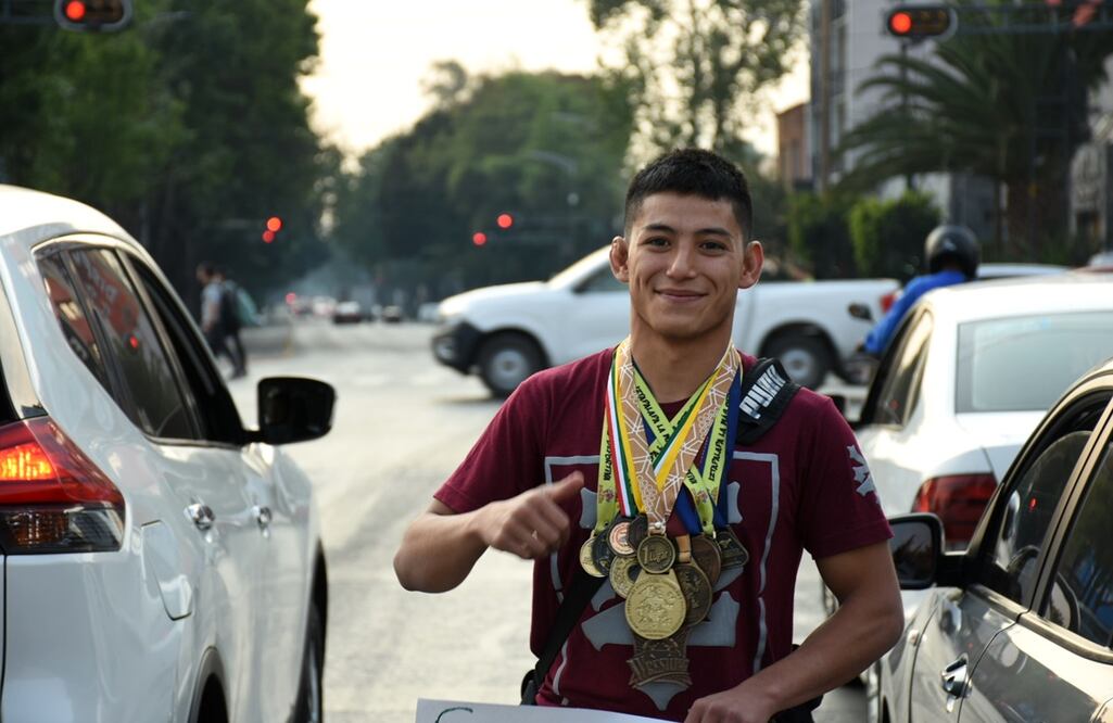 Adrián se cuelga las medallas antes de pasar de coche en coche y con una sonrisa pregunta a los conductores si gustan apoyarlo. FOTOS: Axl Chimal/ EL UNIVERSAL/