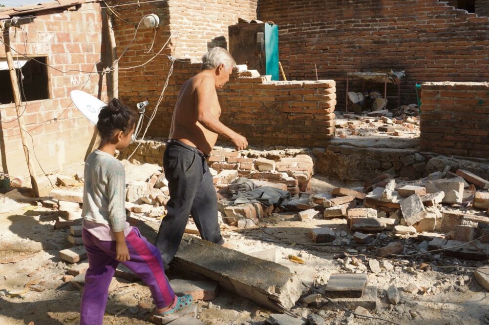 Cristobal Carro camina junto a su nieta Michelle frente a lo que queda de su casa, derrumbada por el sismo, en Santiago Jamiltepec. (EDWIN HERNÁNDEZ. EL UNIVERSAL)