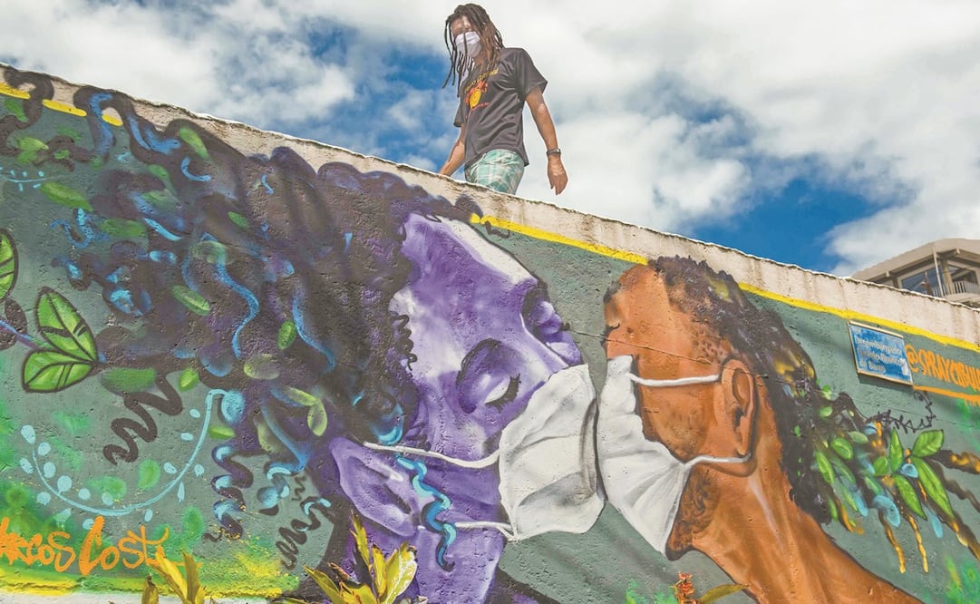 Un brasileño pasa por donde hay un graffiti pintado en la favela Solar de Unhao, en Salvador, el cual muestra a una pareja besándose con cubrebocas en medio de la pandemia del coronavirus. Foto: ANTONELLO VENERI. AFP