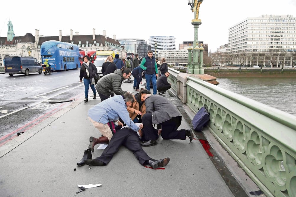 Un grupo de personas atiende a un hombre que resultó herido cuando un individuo en un vehículo arrolló a quienes se encontraban en la banqueta del puente de Westminster, a un costado del edificio del Parlamento (TOBY MELVILLE. REUTERS)