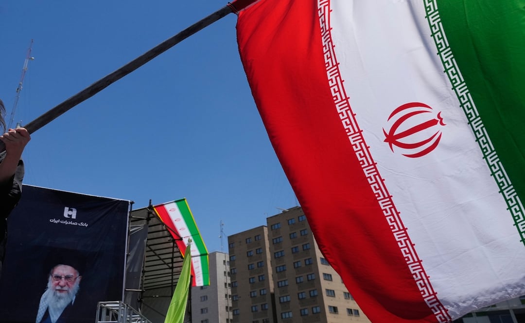 Una persona ondea una bandera de Irán en el centro de Teherán y al fondo puede verse un retrato del ayatolá Alí Jamenei. Foto: AP