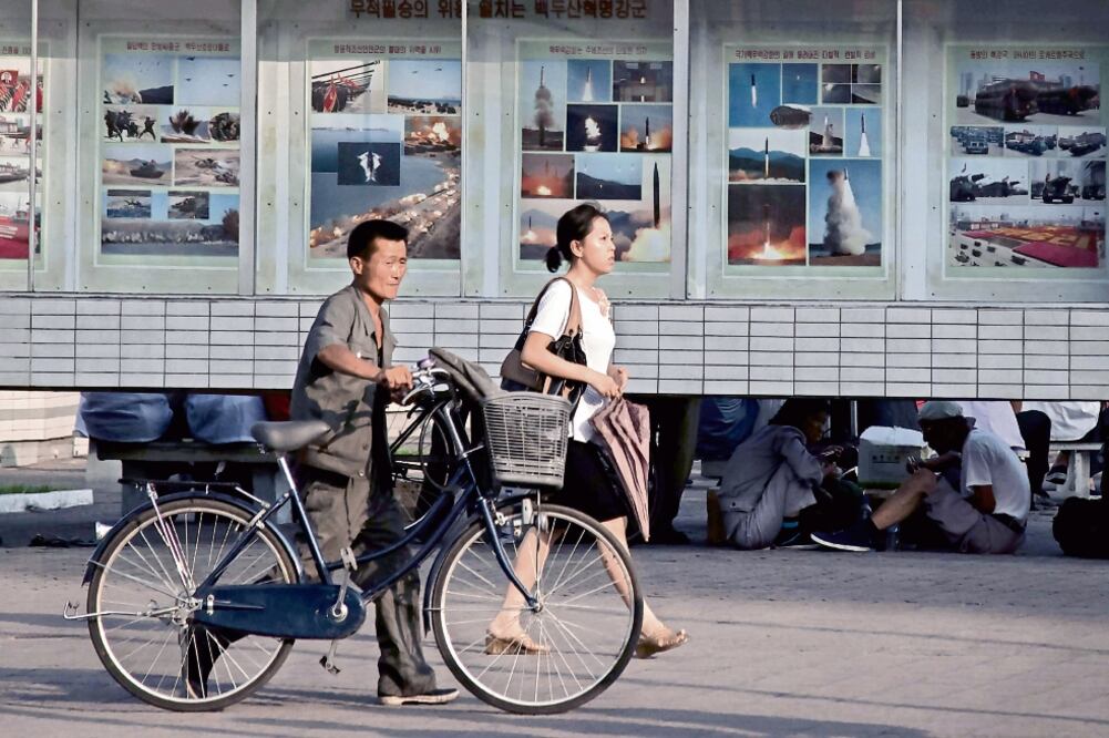 Peatones pasan junto a una exhibición de lanzamientos de misiles y ejercicios militares, en una calle de Pyongyang, la capital norcoreana (ED JONES. AFP)