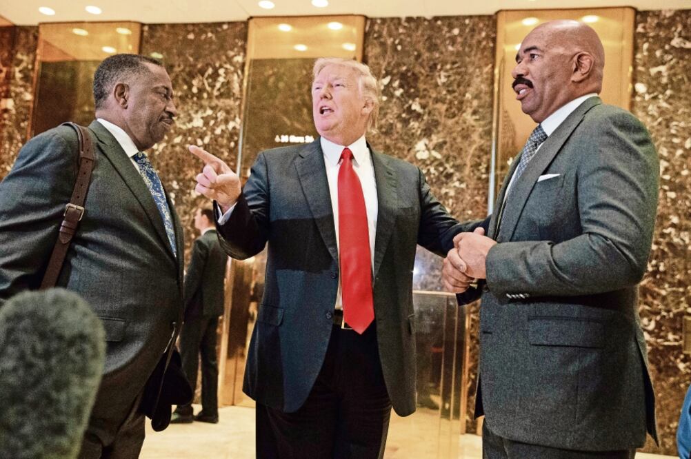El presidente electo de EU, Donald Trump, ayer en el lobby de la Torre Trump, junto con el comediante Steve Harvey (der.) y el empresario Greg Calhoun (izq.) (EVAN VUCCI. AP)