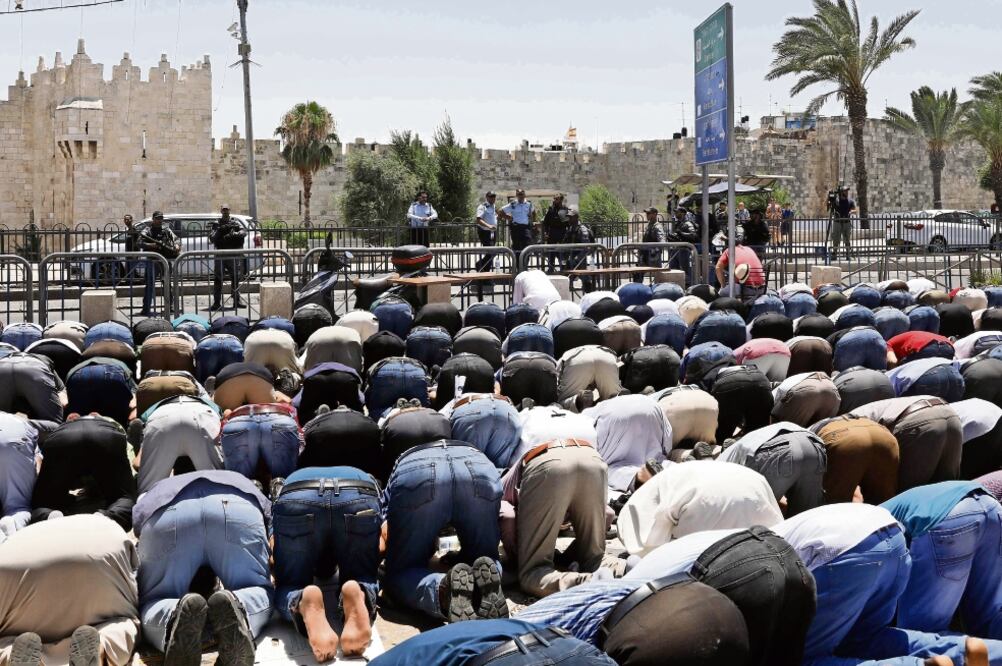 Musulmanes rezan afuera de una de las entradas a la Vieja Jerusalén, tras el cierre ordenado por las autoridades israelíes, poco después del ataque contra policías. La zona será reabierta mañana. (GALI TIBBON. AFP)