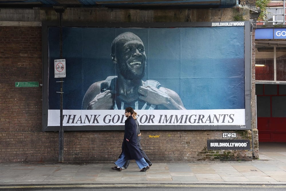 Peatones pasan junto a una publicidad del rapero Stormzy con la leyenda "Gracias a Dios por los migrantes", creada por  el grupo político "Todos Odian a Elon". FOTO: TOBY SHEPHEARD. AFP