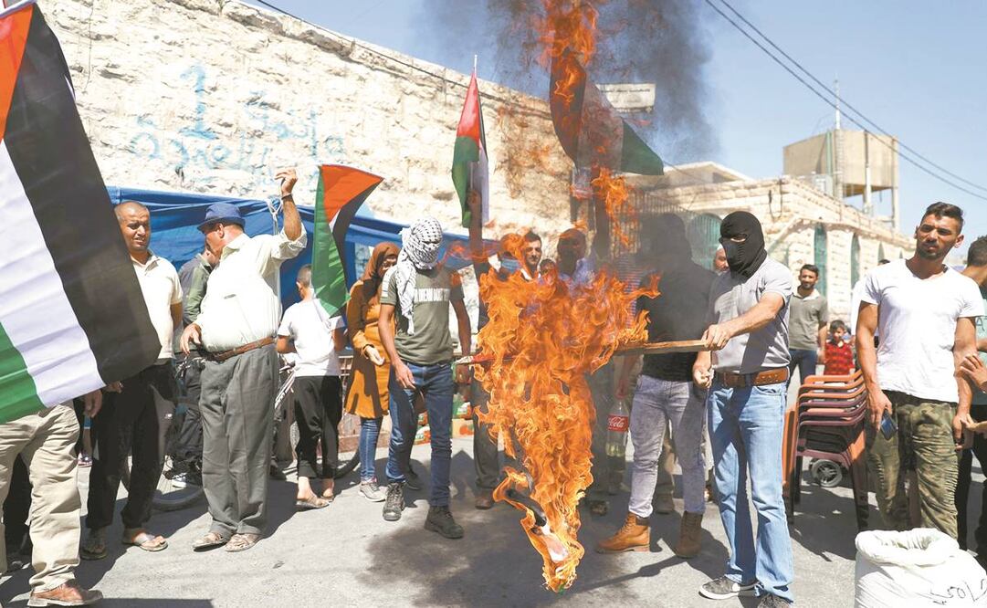 Palestinos, ayer en Yatta, Cisjordania, al quemar una bandera de Emiratos Árabes Unidos, en una protesta contra el pacto de ese país con Israel. Foto: ABED AL HASHLAMOUN. EFE