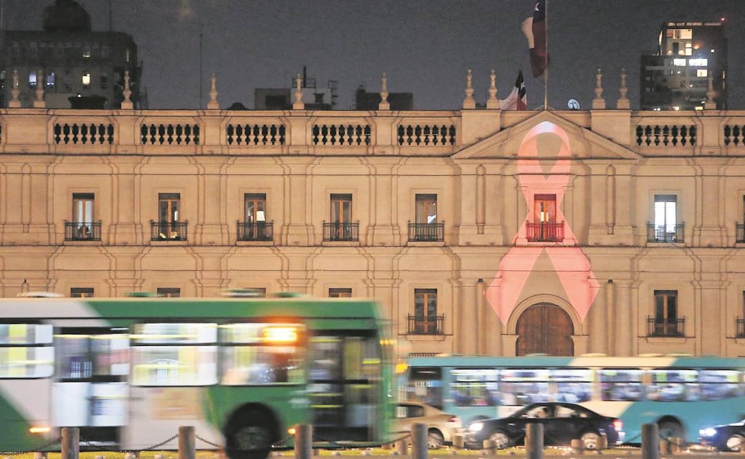 Autobuses pasan frente al Palacio de La Moneda, en Santiago de Chile, iluminado, en 2015, con el Lazo de la Vida, símbolo del VIH/Sida en el mundo.Foto: Archivo/EFE