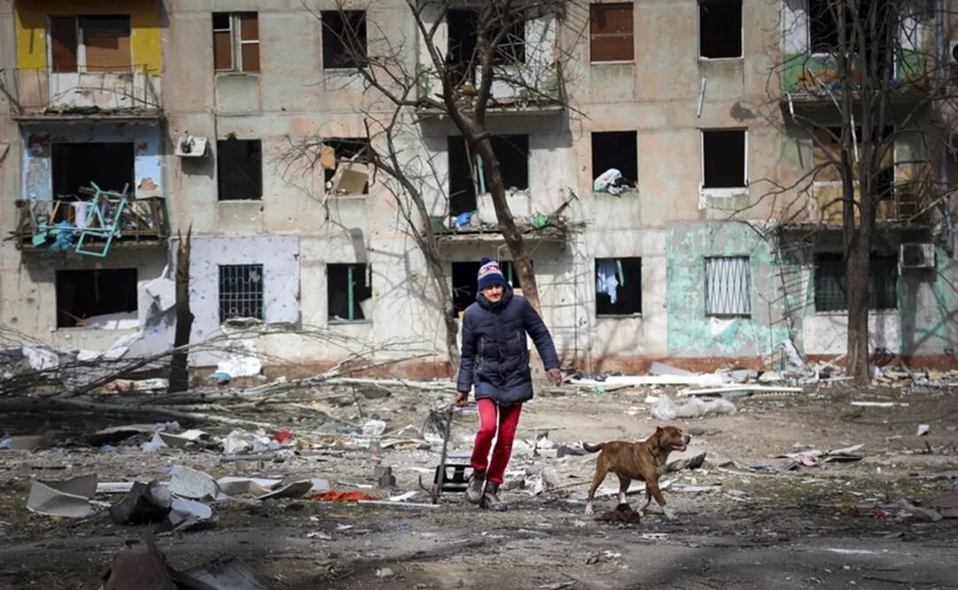 Un hombre camina con su perro cerca de un edificio dañado por los bombardeos de los combates en las afueras de Mariupol.   Foto: AP 