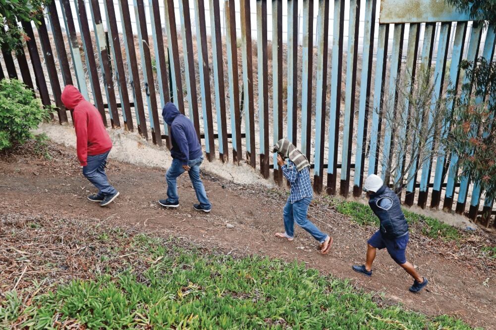 Migrantes caminan junto a una valla fronteriza en el crce entre Tijuana y Estados Unidos. (REBECCA BLACKWELL. AP)
