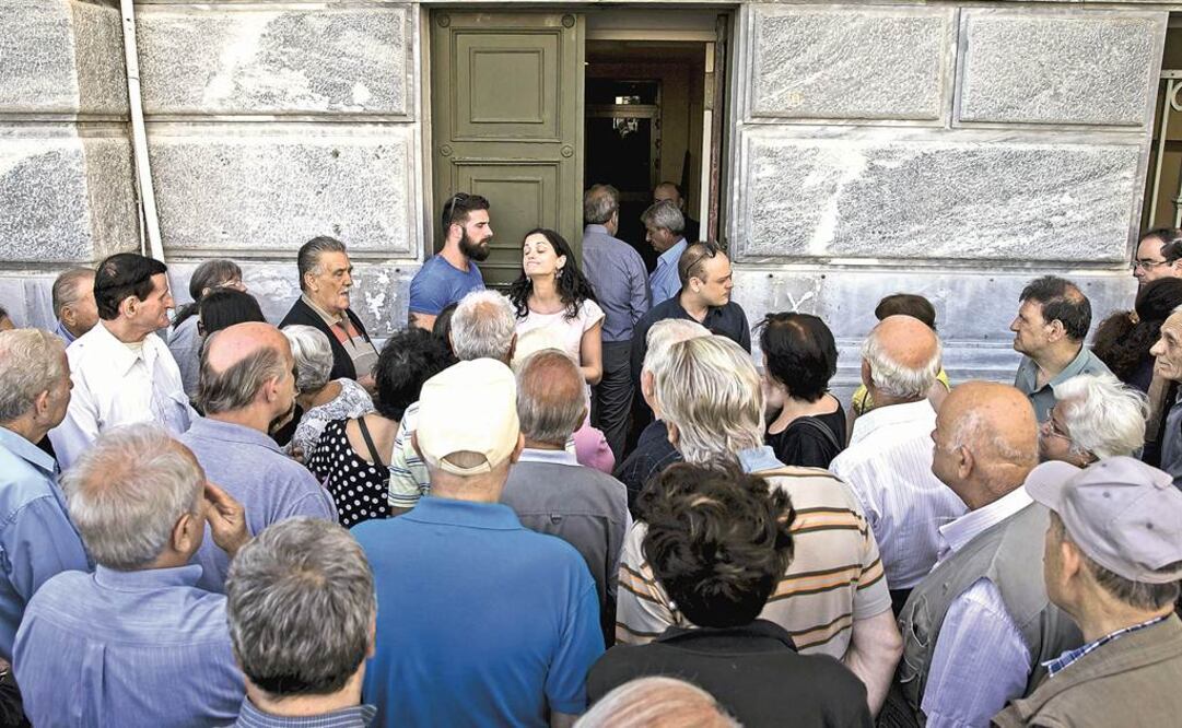 Pensionados griegos hablan con personal de una sucursal del Banco Nacional en Atenas, que ayer permaneció cerrado, al igual que todo los bancos, como parte de las medidas restrictivas ordenadas el domingo por el gobierno