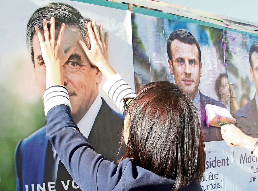 Simpatizantes del conservador François Fillon cubren en Bayona propaganda del centrista Emmanuel Macron, en vísperas de las presidenciales francesas. (BOB EDME. AP)