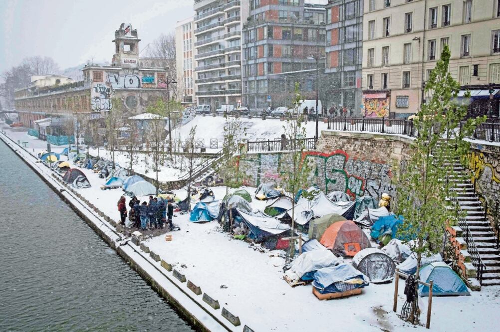 Refugiados afganos buscan calentarse en medio de las nevadas que azotan la capital francesa en estos días. (JOEL SAGET. AFP)