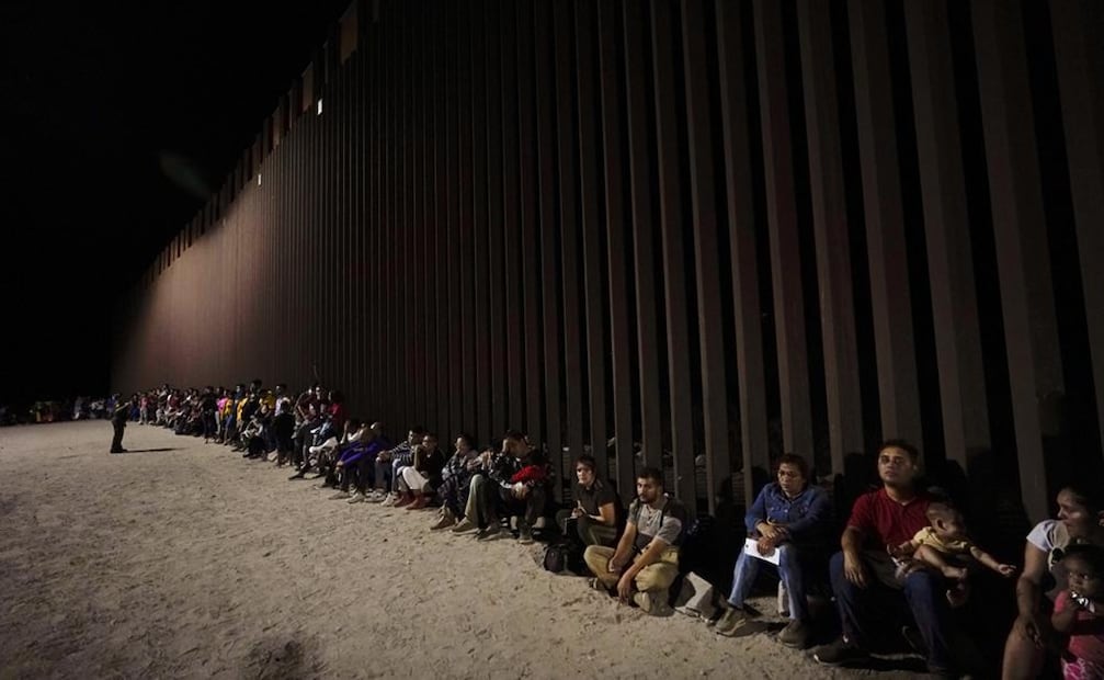 Migrantes esperan junto a un muro fronterizo tras cruzar desde México cerca de Yuma, Arizona. Foto: AP