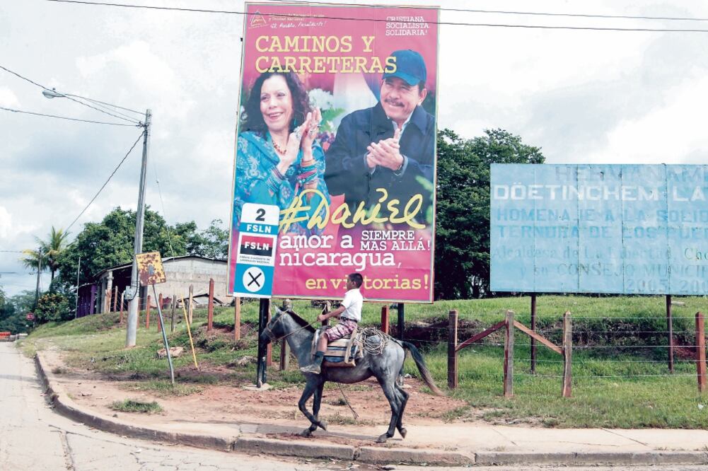 Un niño en su caballo pasa junto a un cartel de propaganda del presidente-candidato Daniel Ortega y su compañera de fórmula y esposa, Rosario Murillo, en La Libertad (OSWALDO RIVAS. REUTERS)