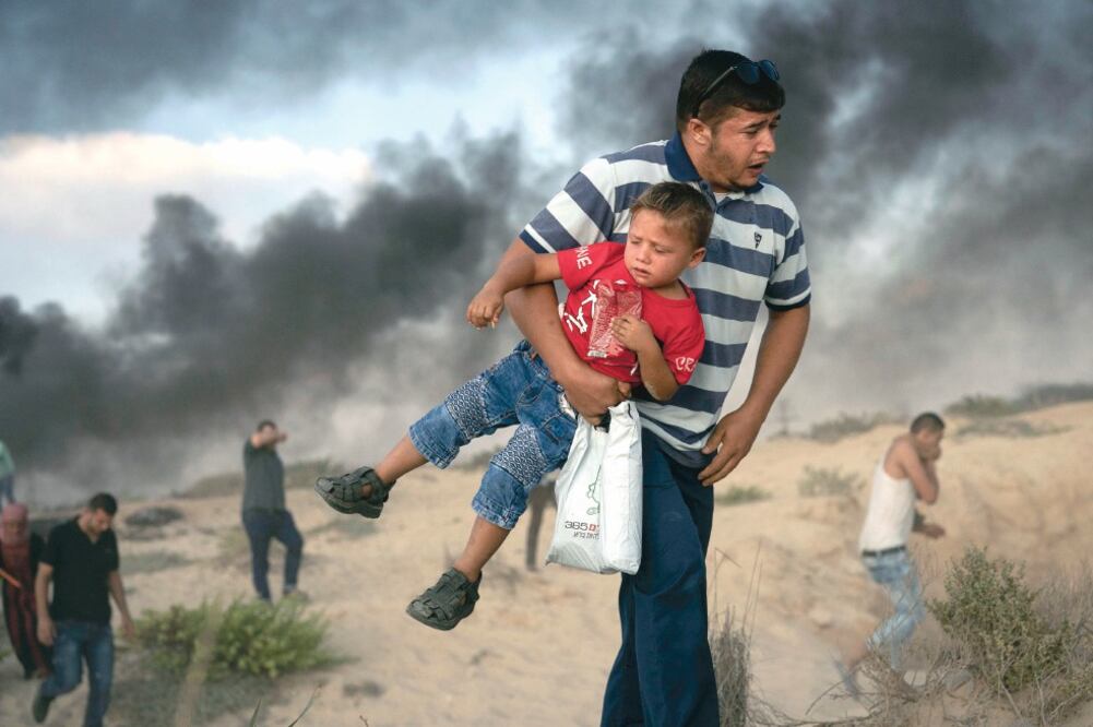 Un manifestante palestino carga a un niño, mientras huye de gas lacrimógeno disparado por soldados israelíes ayer durante una protesta cerca de la frontera. (FELIPE DANA. AP)