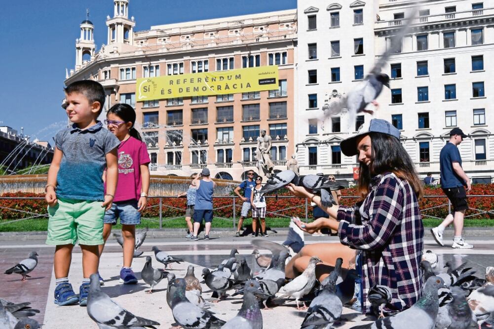 Una mujer alimenta palomas en la plaza Cataluña de Barcelona. En el edificio del fondo, una pancarta que dice: “Sí. Referéndum es democracia”. (LLUIS GENE. AFP)