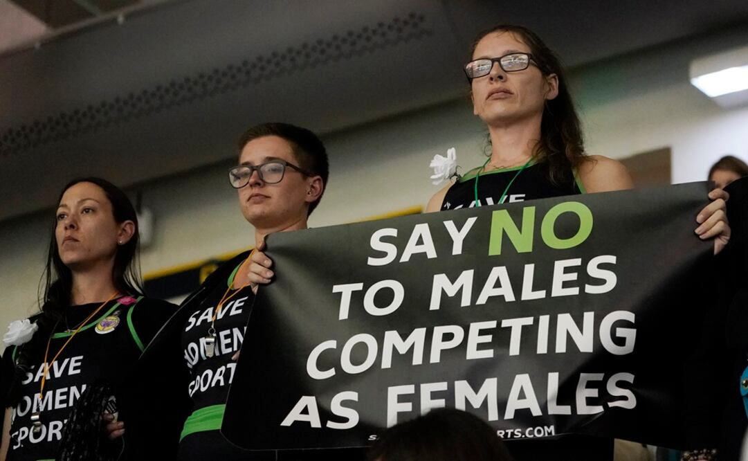 Manifestantes, uno con un cartel, se paran mientras la atleta transgénero de Pensilvania, Lia Thomas, compite en la final femenina. Foto: AP