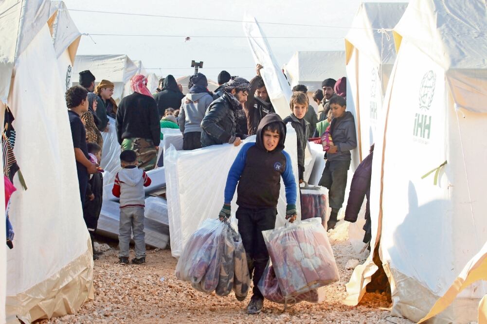Un sirio desalojado de Aleppo carga sábanas que recibió en el campamento para refugiados de al-Kamouneh, en la provincia de Idlib (AMMAR ABDULLAH. REUTERS)