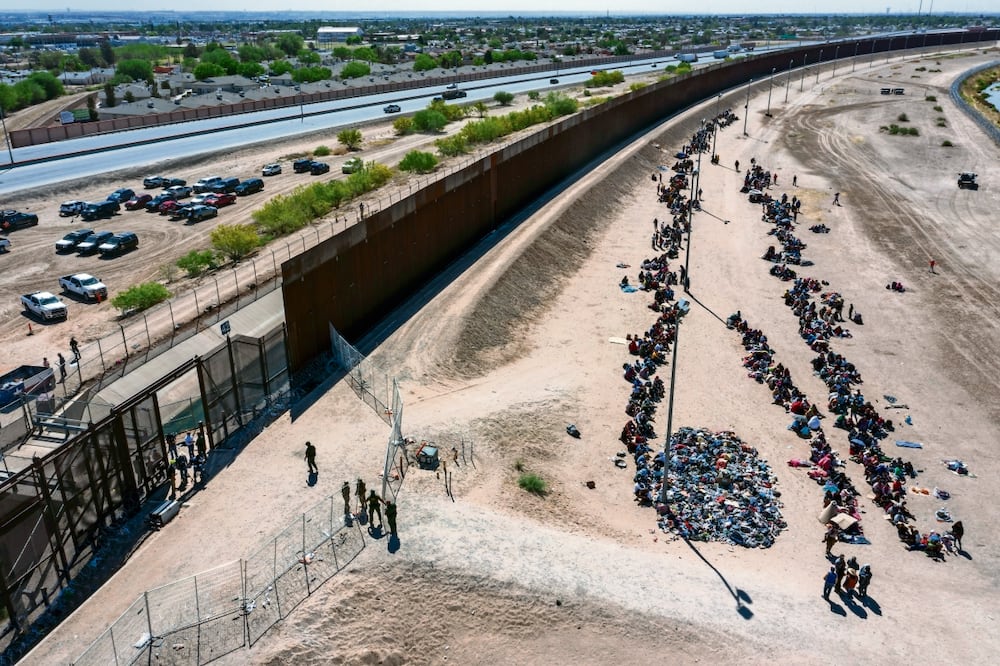Migrantes forman filas fuera de la cerca fronteriza esperando ser transportados a una instalación de la Patrulla Fronteriza en El Paso, Texas.
