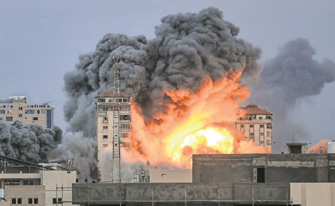 Personas paradas en una azotea observan cómo una bola de fuego y humo se eleva sobre un edificio en la ciudad de Gaza. Foto: AFP