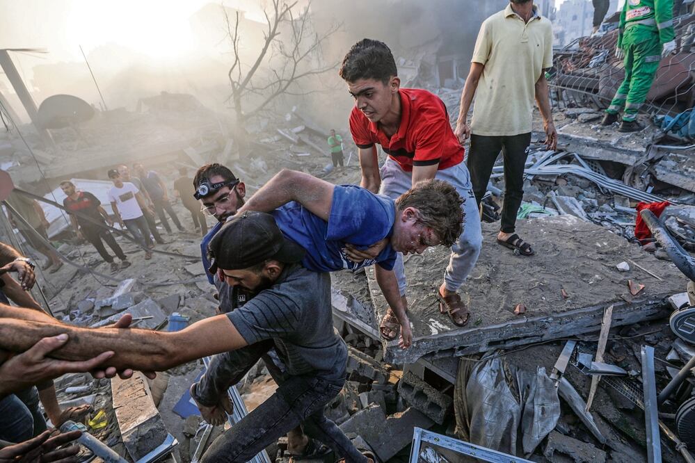 Un palestino carga a un niño herido, en medio de los escombros de una zona destruida tras los ataques aéreos israelíes en Gaza. Foto: EFE